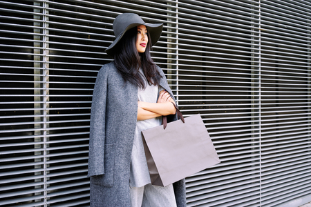 young beautiful stylishly-dressed Asian girl posing and holding a blank paper bag with empty space for your text or logoの写真素材