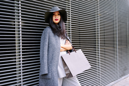 young attractive stylishly-dressed Asian girl posing and holding a blank paper bag with empty space for your text or logoの写真素材