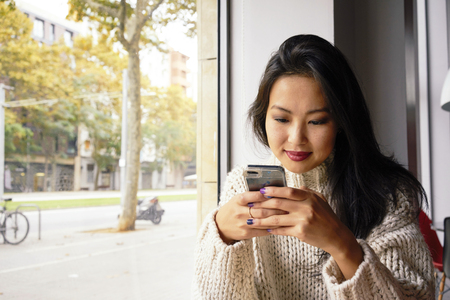 Young Asian Girl chatting via digital tablet device during breakfast in coffee shop.Portrait of a pretty Asian woman reading message on her cell telephoneの写真素材