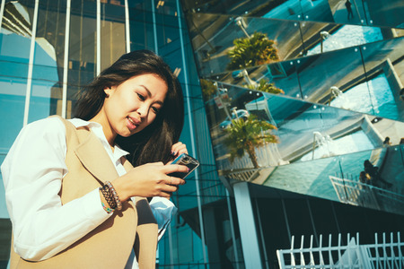 Pretty young Asian businesswoman uses modern smart-phone outside the office. portrait of a beautiful Asian female students recorded a video for her video blogの写真素材