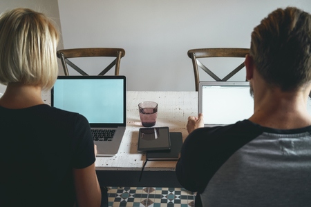 Young beautiful woman and young brutal man working with laptop and other devices at office tableの写真素材