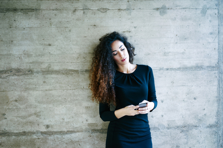 young attractive girl sending message with smartphone on the background of concrete wall with blank copy space for your text and design.Beautiful young business woman using a cell phoneの写真素材