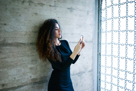 young attractive businesswoman sending message with smartphone on a concrete wall background.Beautiful young business woman using a cell phoneの写真素材