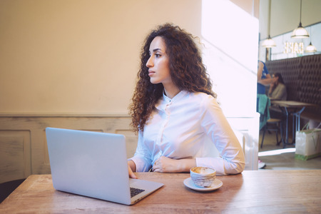 young attractive girl with curly hair working with a laptop computer in a coffee-shop.Beautiful female student searching information on the Internetの写真素材