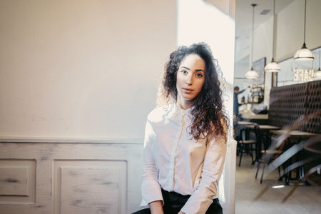 young beautiful business woman sitting in coffee-shop on a white wall background with blank copy space for your information or designの写真素材