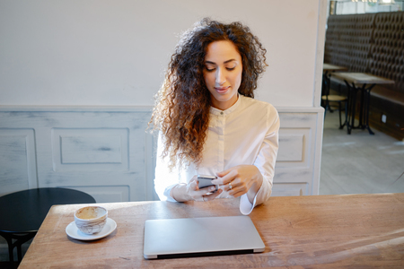 young beautiful businesswoman writes a message on her smart-phone during the lunch break. Attractive student doing homework in a cafe.の写真素材