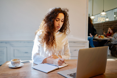 Young attractive business woman holds a job interview in a cafe during the lunch break. businesswoman searching for information on the Internet and makes notes in a notebookの写真素材