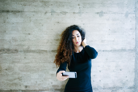 young attractive girl making selfies on the background of concrete wall with blank copy space for your text and design.Beautiful young business woman using a cell phoneの写真素材