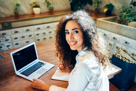 Attractive girl working in a cafe with a laptop during lunch. young business woman searching for information on the Internet and makes notes in a notebookの写真素材