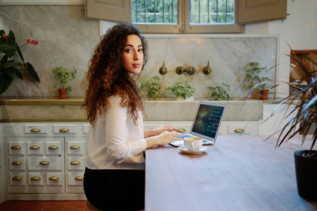 Young attractive business woman checks e-mail on her laptop while sitting in a cafe.Beautiful female freelancer drinking coffee and typing on a keyboard in a coffee-shopの写真素材
