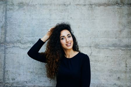 Young smiling girl with long curly hair while standing against gray concrete wall with copy space area for your text messageの写真素材