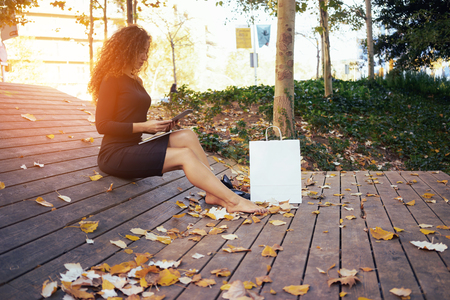 young beautiful woman making online purchases during the lunch break while sitting in the park.standing next to a white blank paper bag for your text or designの写真素材