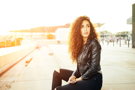 Portrait of fashionable well dressed woman with long curly hair posing outdoors and looking away. flare lightの写真素材