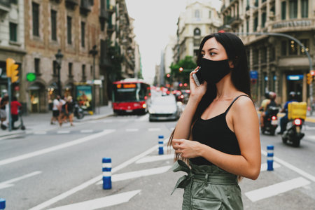 Shot of young woman wearing a respirator mask for health protection during the coronavirus outbreak. Stylish girl talking with the relative on her mobile phone while crossing the street with a trafficの写真素材