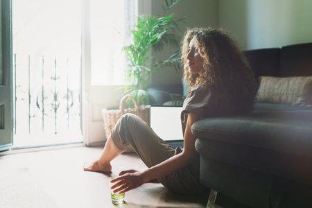 Back view of female using netbook with blank copy space screen for your text message or promotional content. Young woman holding laptop computer while sitting on a floor beside the sofa at home.の写真素材