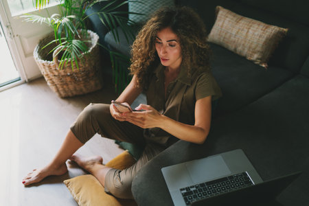 Entrepreneur female checking bank account online on a mobile phone. Attractive woman shopping online using smartphone while sitting home during self-isolation. Successful designer reading emails.の写真素材