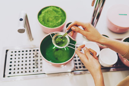 View from the top closeup photo of a green matcha tea making process. Woman's hands holding a strainer and a spoon while preparing a japanese green tea in a coffee shop. Tea ceremony in a cafe.の写真素材