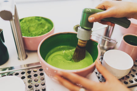 Process of a matcha powder whipping with a modern electric whisk. Barista making natural foamy...