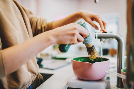 Process of making traditional japanese matcha tea. Barista adding water in a bowl for the matcha tea. Female's hand holding modern electric whisk for whipping the matcha powder in coffee shop.の写真素材