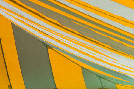 Corner of a well used yellow and gray striped picnic awningの写真素材