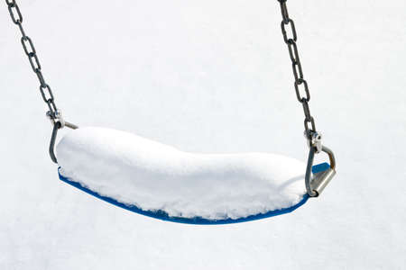 Blue playground swing cover in fluffy white snowの写真素材