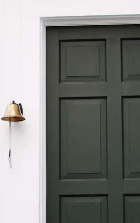 A brass bell hangs next to the green door of a historic buildingの写真素材