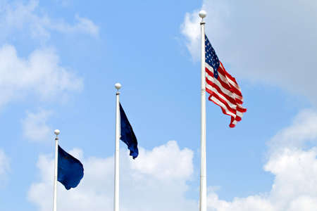 United States flag and two blue flags in a breeze against a scattered cloud skyの写真素材