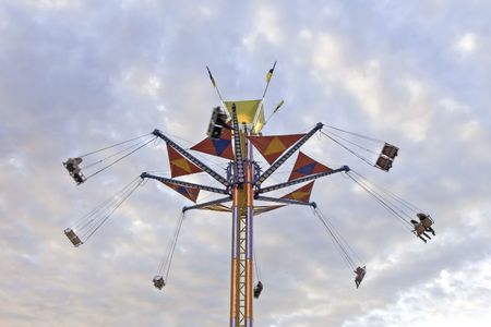 A tower county fair swing ride against a colorful evening sky, the motion creating a slight blur to...