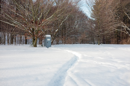 A curved path in deep snow leads to a portable toilet at the edge of a forest.の写真素材