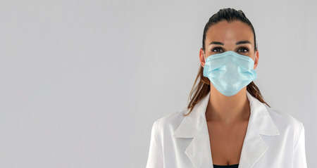 Attractive female doctor with virus protection mask looking straight ahead and white background.の写真素材