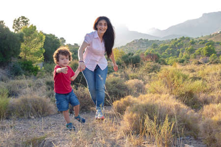Mother and son playing jogging in the field on a day out holding hands and laughingの写真素材