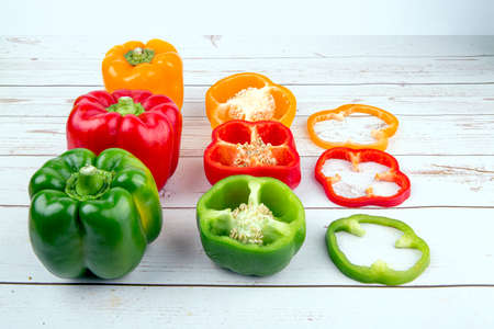A combination of red, yellow and green peppers on a wooden table, placed in a formation of whole,...