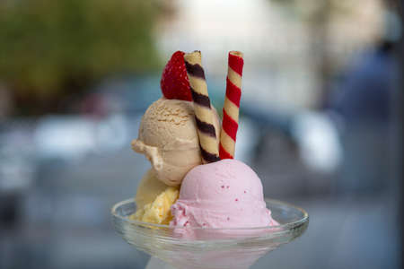 three scoops of ice cream of different flavors and colors in a glass with unfocused background,