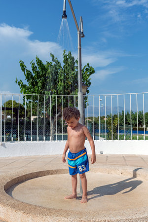 Funny little boy taking a shower in the pool, looking down to the ground as the water falls on him.の写真素材