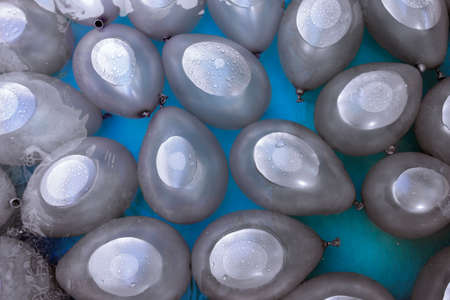 silver-colored water-filled balloons partially submerged and with droplets on their surfaceの写真素材