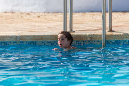 little boy 4-5 years old having fun in the pool inside the water starting to swim