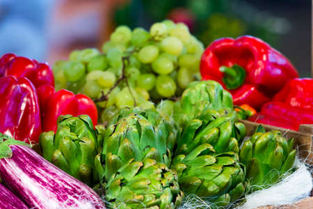 close-up photograph of a set of natural foodstuffs on display, peppers, watercress, artichoke, grapes.の写真素材