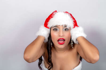 young brunette woman with Santa Claus hat and gloves, hands on head and expression of shock.の写真素材