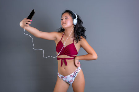 young chinese girl in bikini taking selfie while listening to music with headphones