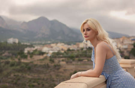 Woman in polka dot dress, leaning on the balcony railing with beautiful viewの写真素材