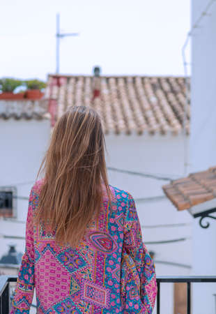 blonde woman seen from behind on balcony overlooking rural village streetの写真素材