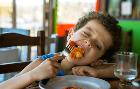 beautiful curly haired boy eating tortellini in restaurantの写真素材