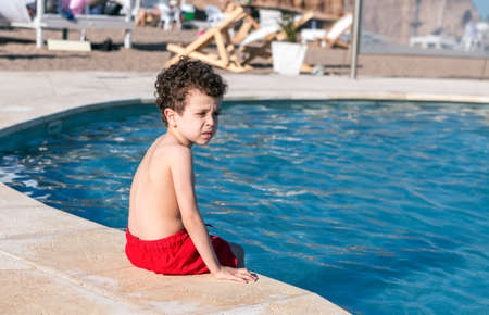 curly-haired boy sitting at the edge of the poolの写真素材