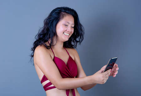 chinese woman in bikini looks at smart phone happy and funnyの写真素材