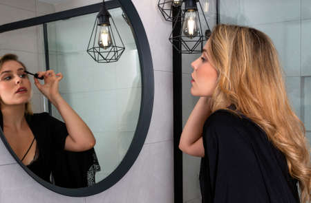 beautiful blonde making herself up in the bathroom in black lingerieの写真素材