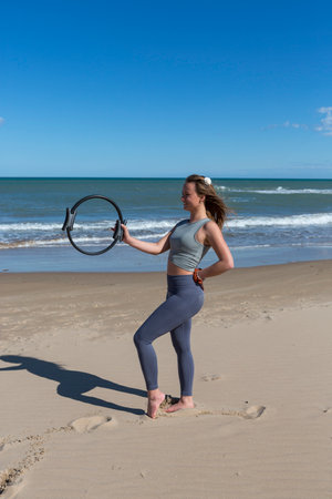 beautiful athlete posing with pilates ring at the beachの写真素材