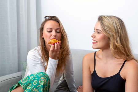 beautiful girl eating a bun and her girlfriend looks at her smilingの写真素材