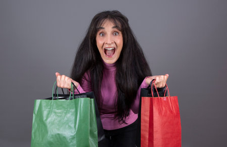 beautiful woman in her 40's looking at the camera screaming with shopping bags in her handsの写真素材