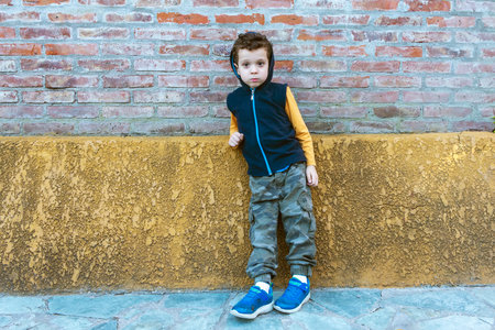 boy in hooded sweatshirt and camouflage pants leaning against brick wallの写真素材