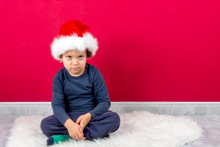 funny boy with serious expression sitting with christmas hatの写真素材